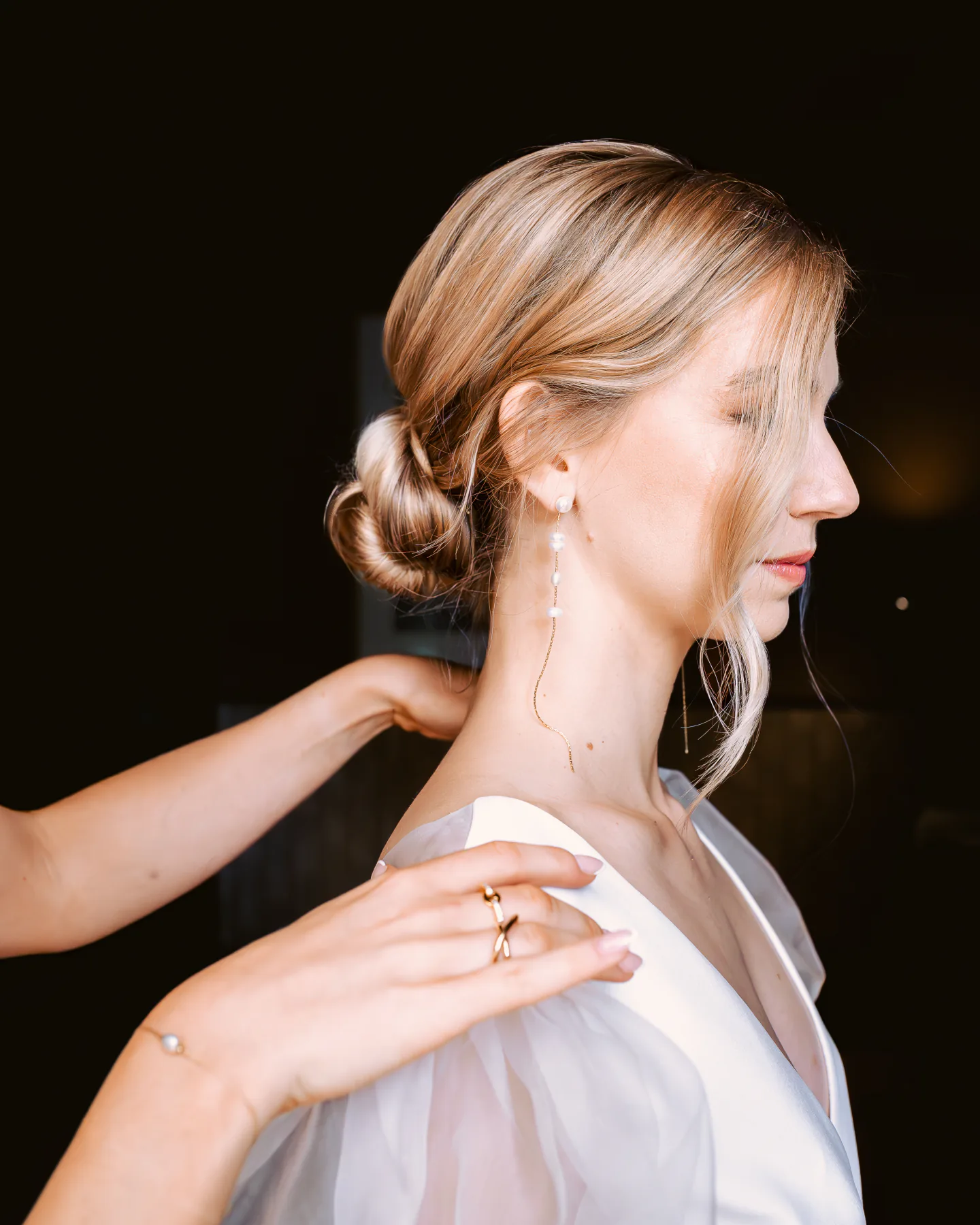 Bridal portrait in profile, hair in a low bun, with a hand resting on her shoulder