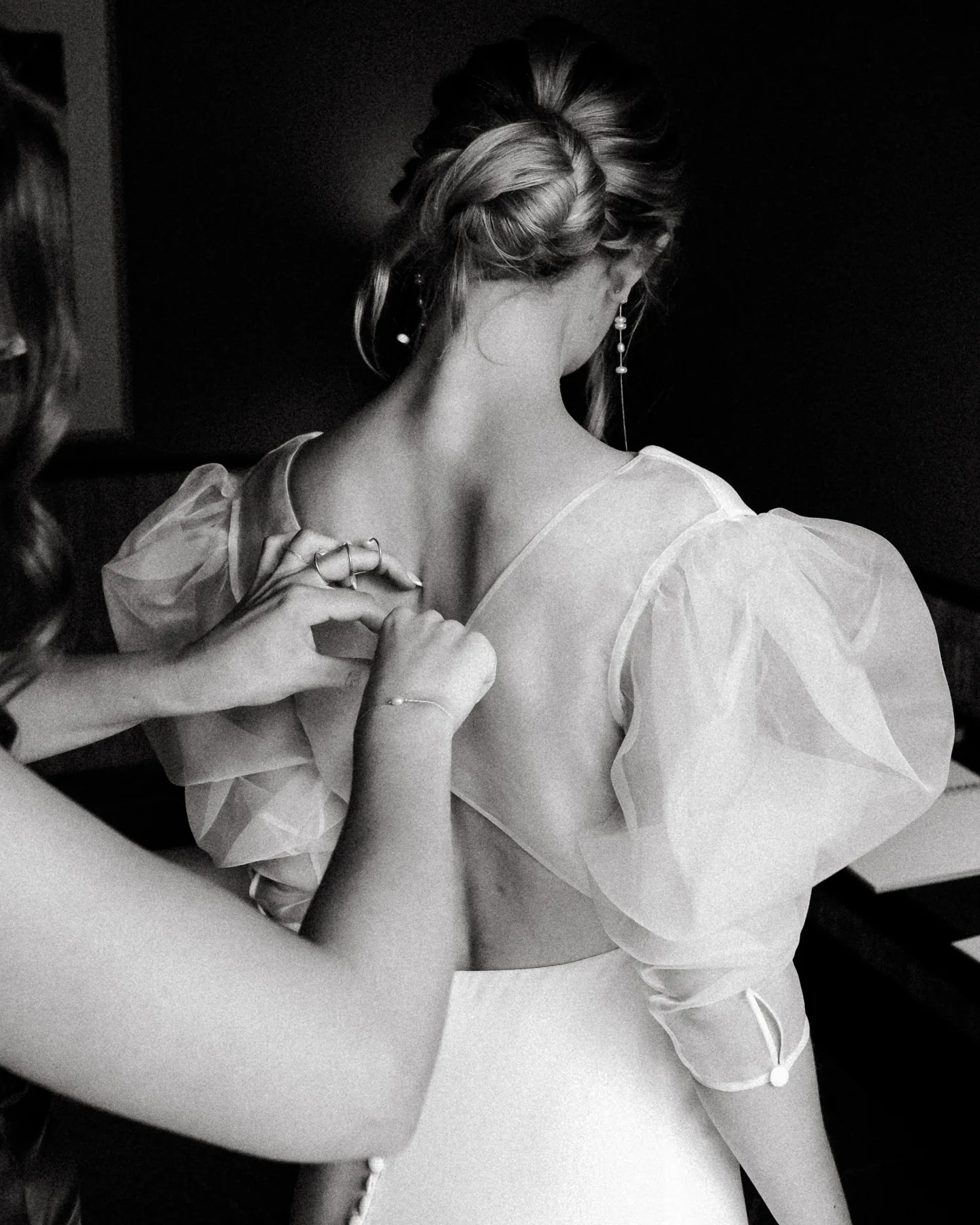 Black-and-white detail of the bride’s back, her bridesmaid fastening the buttons