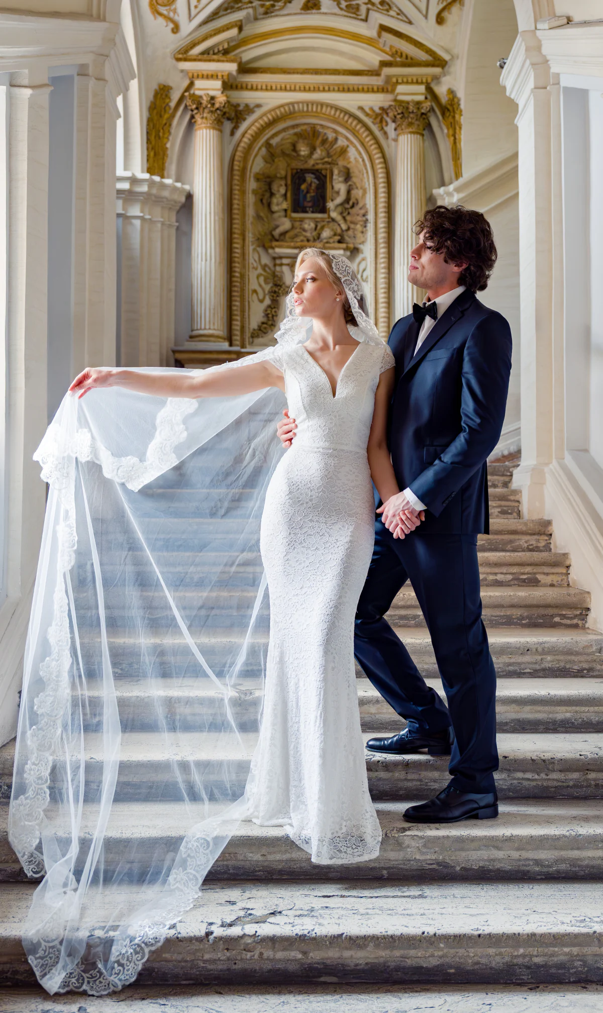 The bride and groom on a stone staircase, her long veil lifted by the wind