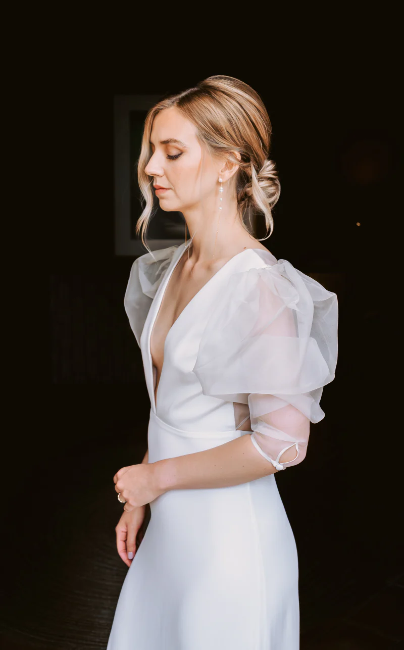Portrait of the bride in profile, her hair in a soft bun, in a white dress with a plunging neckline