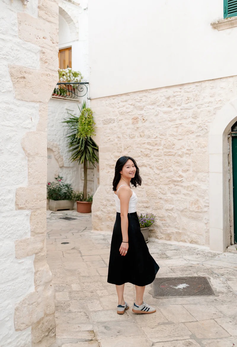 A woman in a black skirt walking through a whitewashed alley in Monopoli