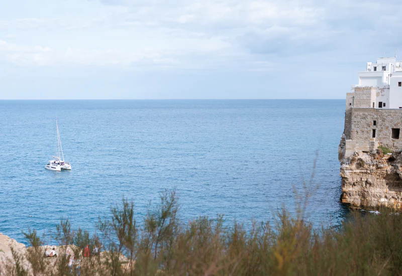 The sea and the white town of Monopoli on its cliff, with a sailboat