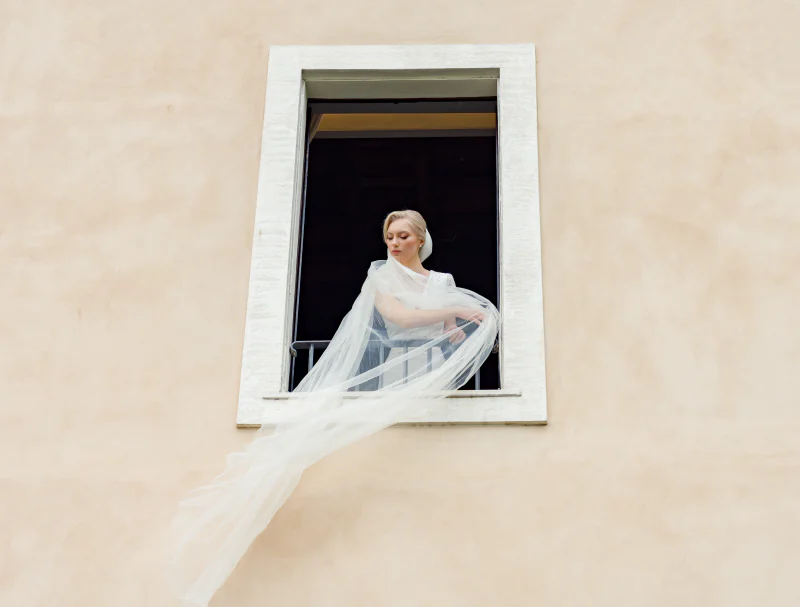 Bride at a window, her long veil lifted by the wind