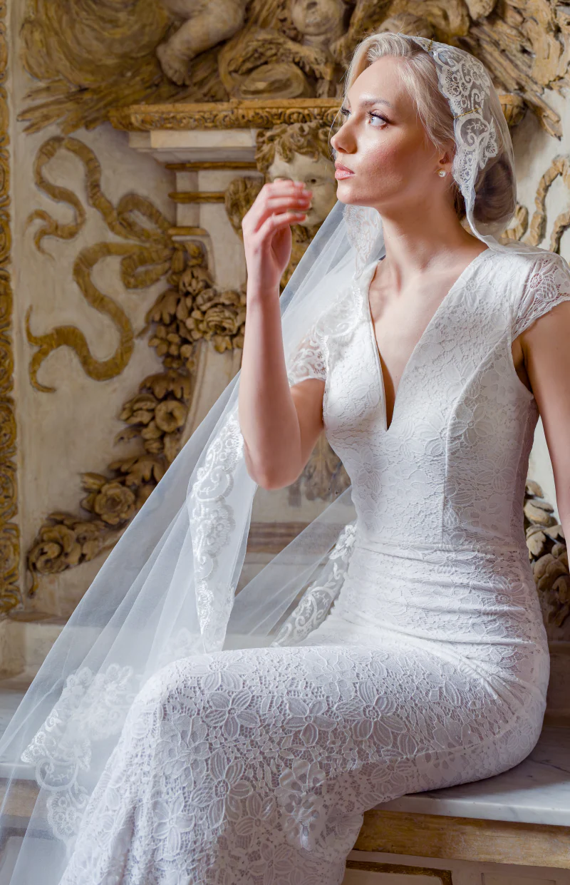 Bride in a lace gown and veil, seated beneath a gilded ceiling