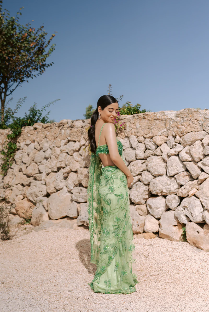 Woman in a green embroidered sari beside a stone wall