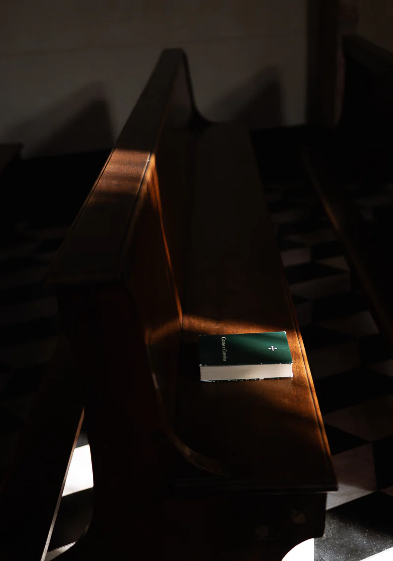 A small green book on a church pew, in a shaft of light