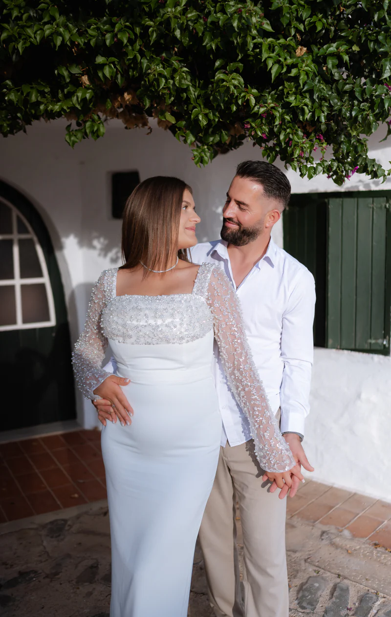 Couple in white smiling at each other in a whitewashed courtyard
