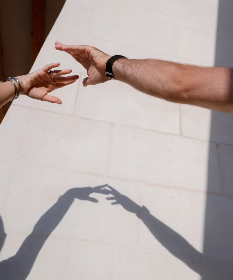 Two hands reaching out, their shadows on a white wall