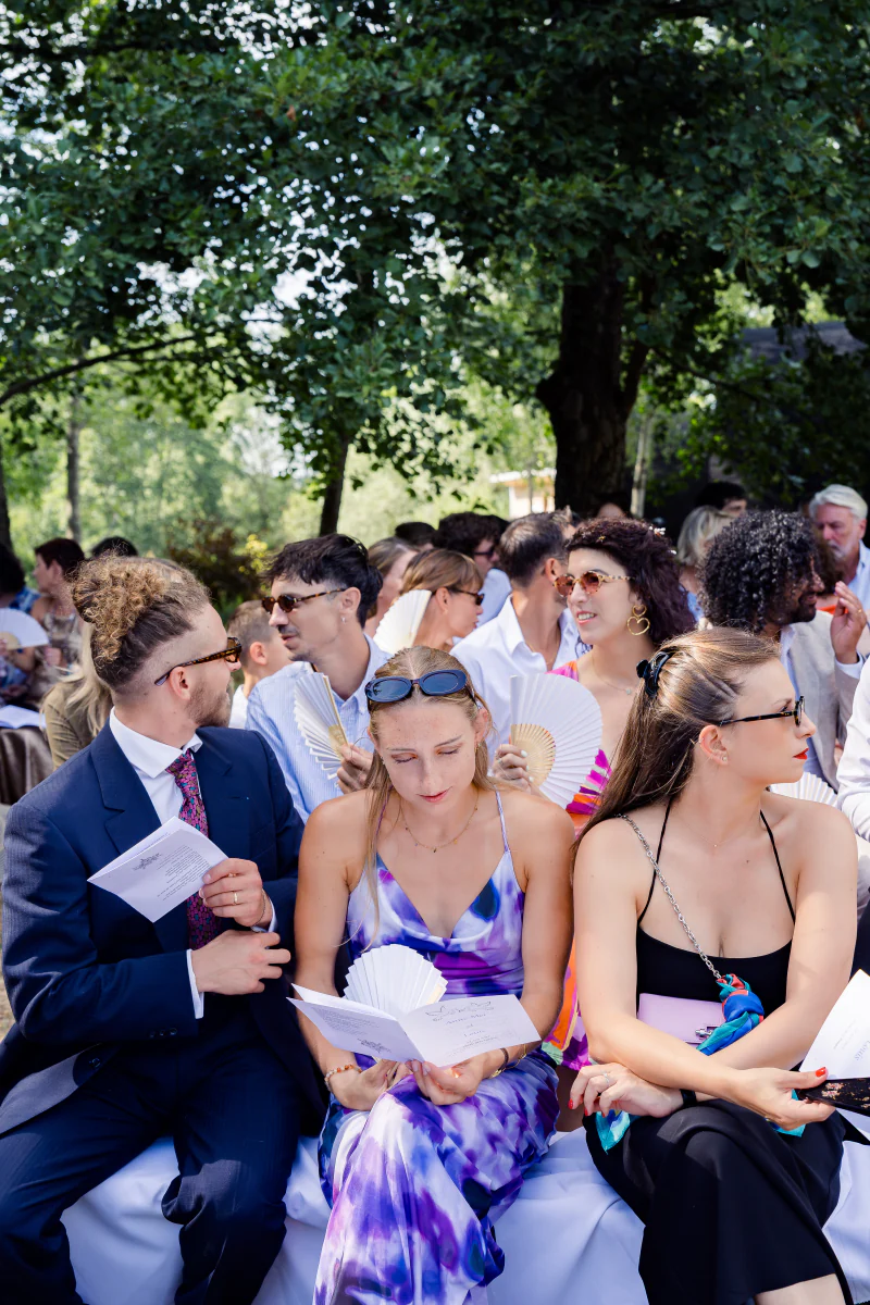 Wedding guests at the outdoor ceremony, reading the programme