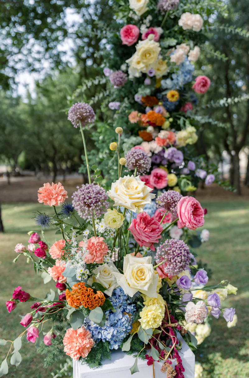 Tall floral arrangement of roses, delphiniums and dahlias in a garden