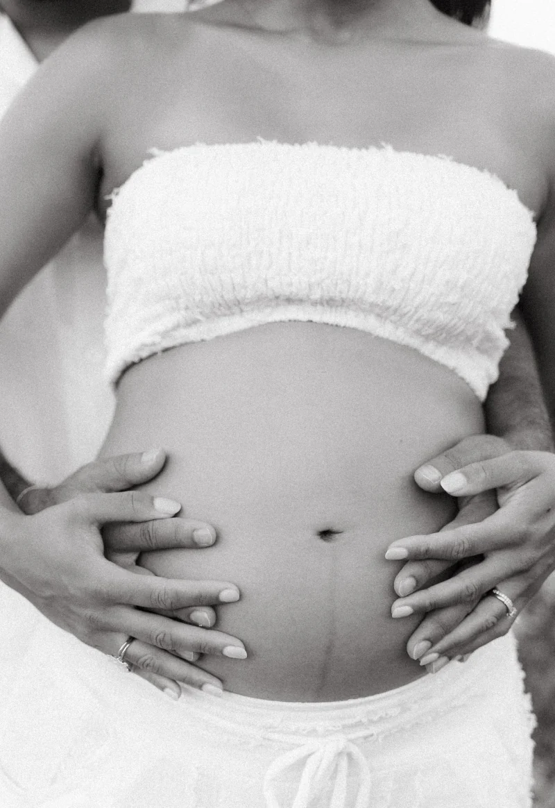 Black-and-white detail of a pregnant belly held by two hands