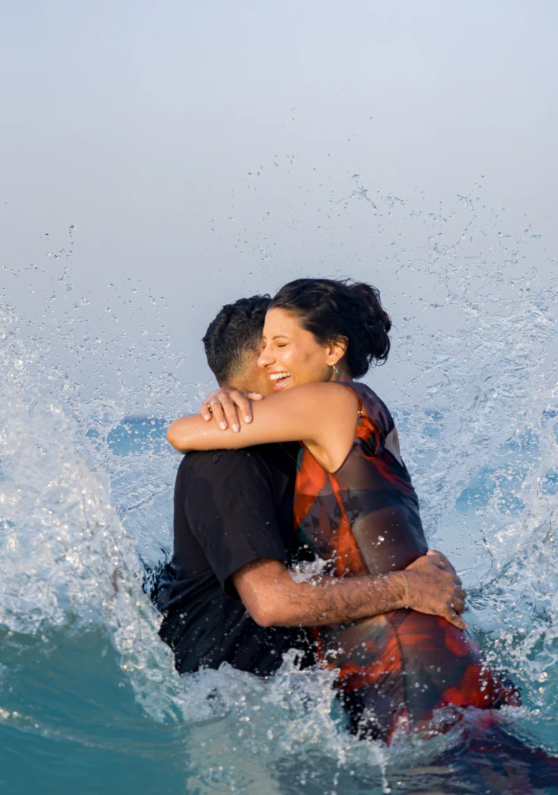 Couple embracing as a wave splashes around them